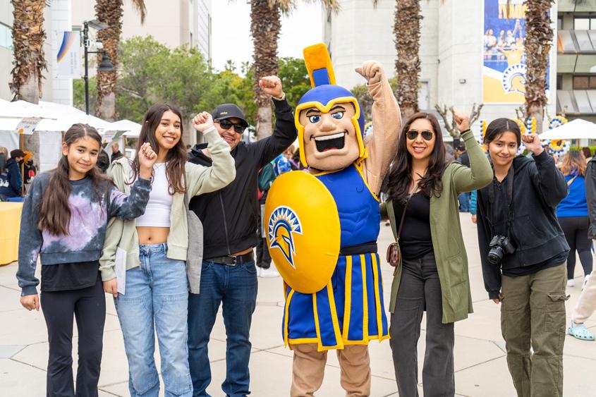 Admitted student witht their family members pose with Sammy Spartan with a fist pump in the air.