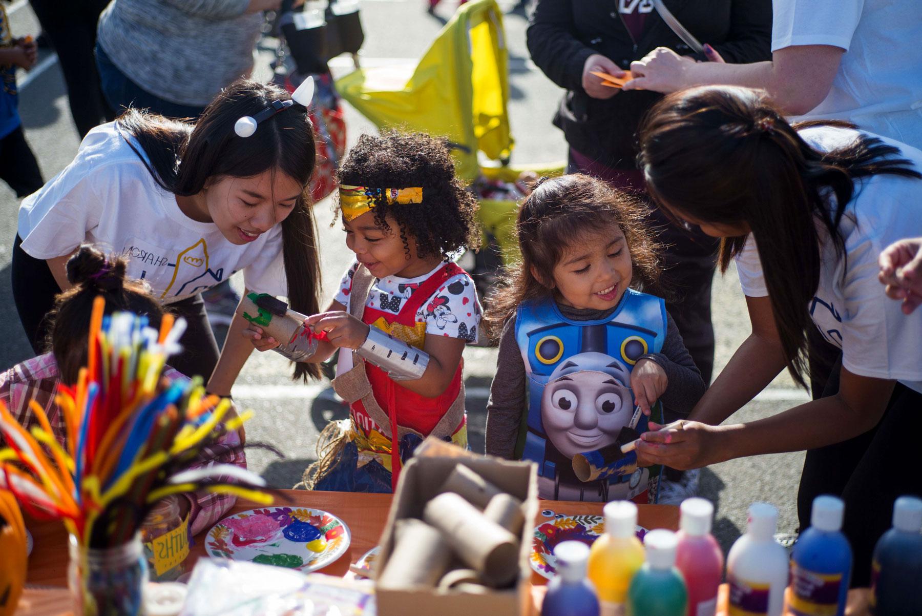 Student volunteers help two kids with their arts and crafts during a halloween event.