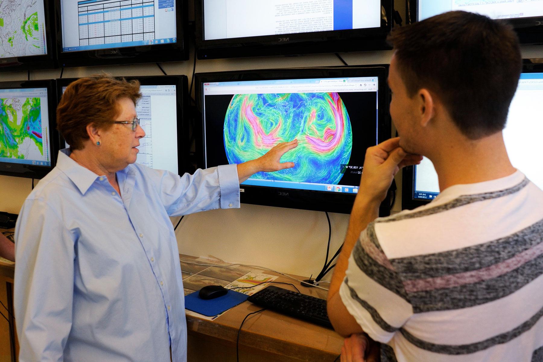 A professor points to a screen showing weather patterns to a student.