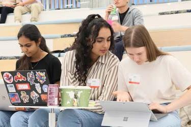 在圣何塞州立大学，三名国际学生一边在电脑前学习，一边听讲座.